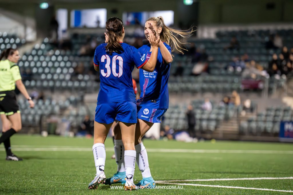 Sienna Dale and Emily Minett celebrate a goal during the 2023 NPL NSW Women's Round 12 game between Manly United and Bankstown City at Cromer Park. Photo credit: Jeremy Denham