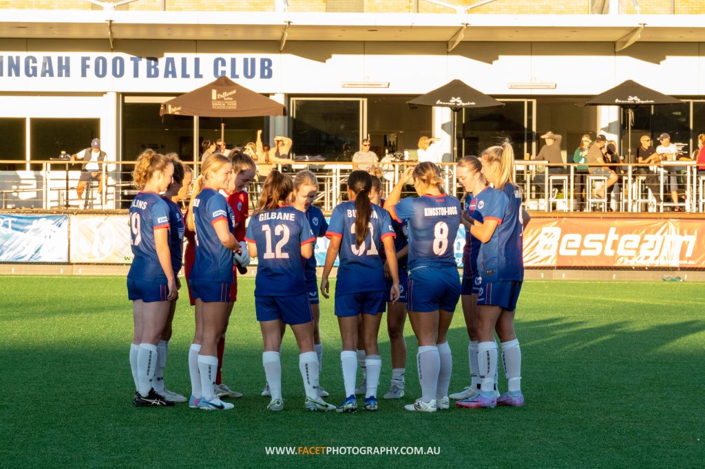 Manly United huddle before their 2023 NPL NSW Women's Round 6 game against Northern Tigers at Cromer Park. Photo credit: Jeremy Denham